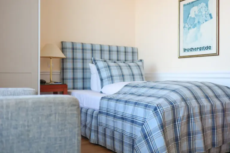 Behagliches Einzelzimmer im Seeschlösschen Timmendorfer Strand mit blau kariertem Boxspringbett, klassischer Einrichtung und maritimem Flair.