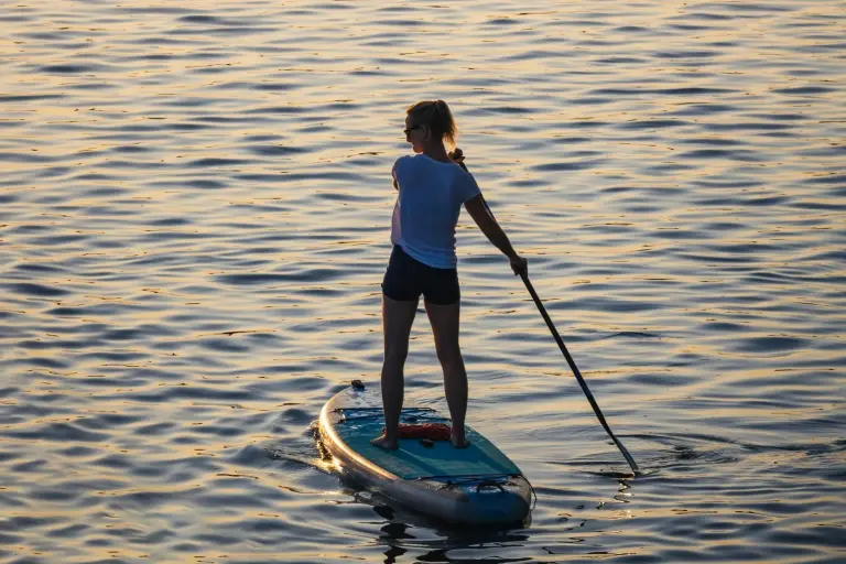 Eine Frau paddelt im Sonnenlicht über ruhiges Wasser und zeigt, wie vielfältig Wassersport an der Ostsee sein kann.